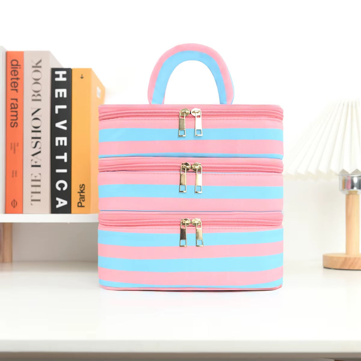 Pink and blue striped bag on a shelf with books and a candle in the background