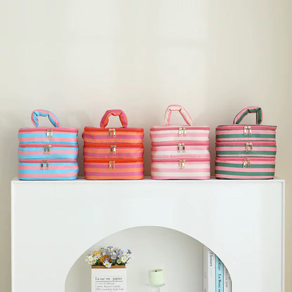 Four striped fabric storage bags with gold-tone zippers and handles, displayed on a white shelf against a light beige wall.