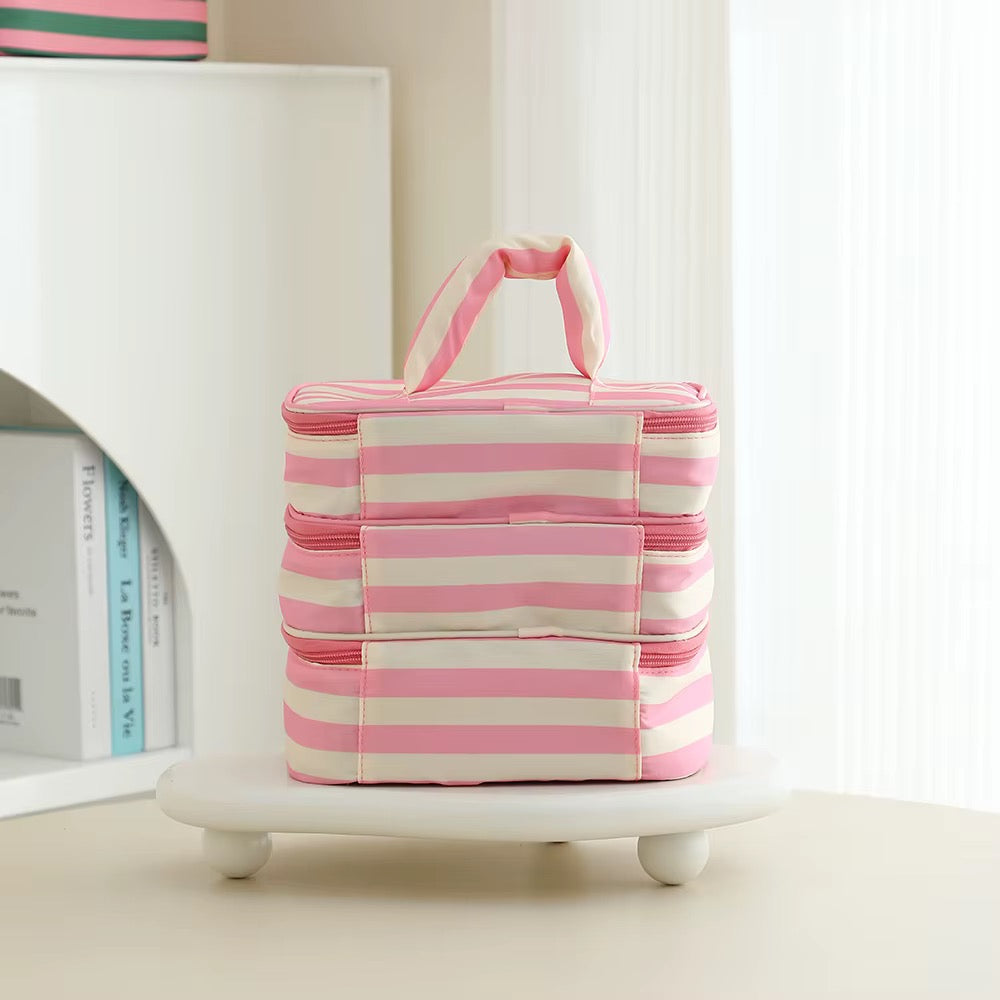 A stack of three pink and white striped insulated lunch bags with top handles, displayed on a small white pedestal in a bright, modern room setting.