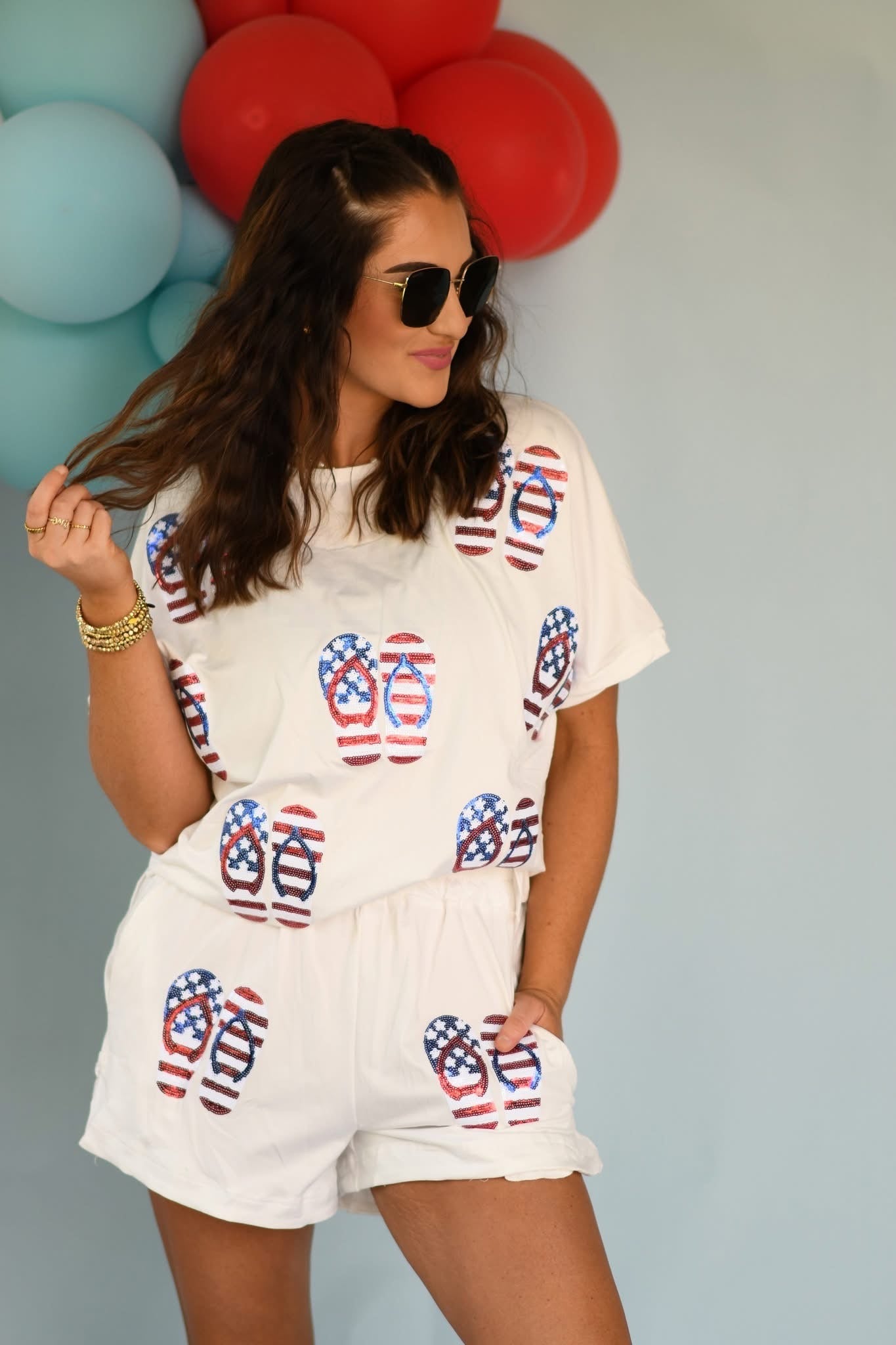 Woman wearing a white outfit with red, white, and blue flip-flop pattern in front of balloons.