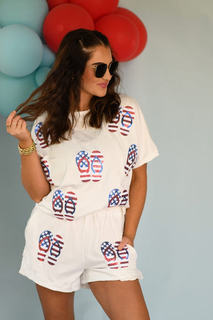 Woman wearing a white outfit with red, white, and blue flip-flop pattern in front of balloons.