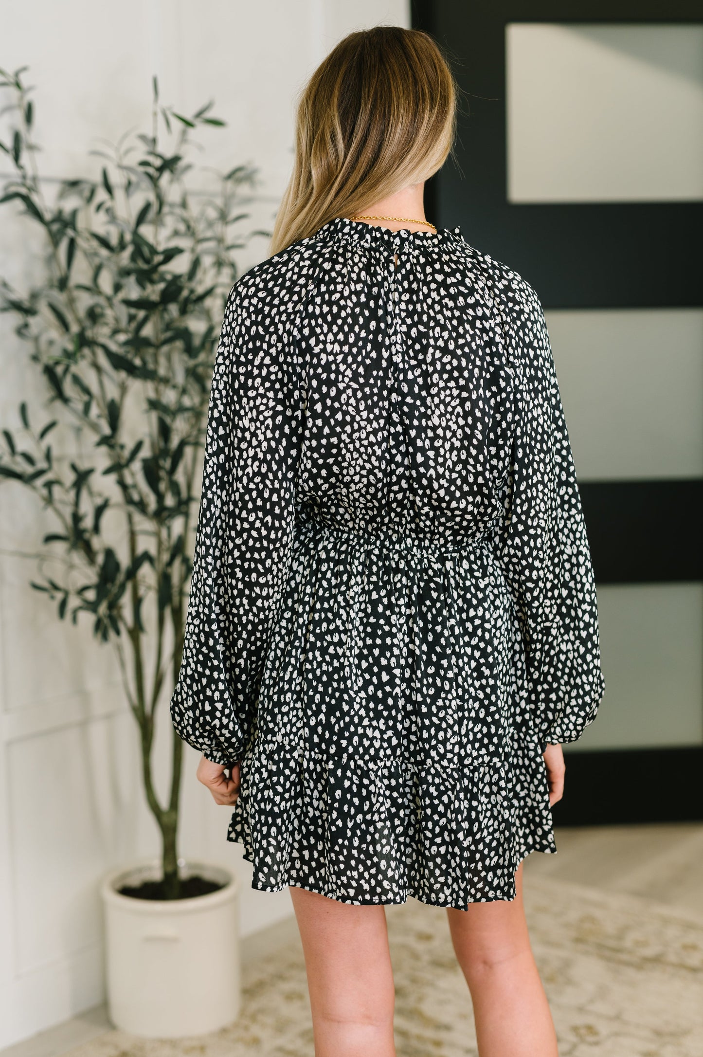 Woman wearing a black and white patterned dress in a room with a plant and wall art.