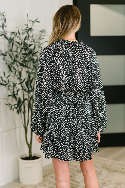 Woman wearing a black and white patterned dress in a room with a plant and wall art.
