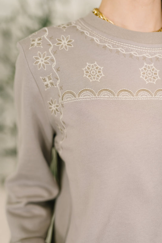 Close-up of a beige sweater with floral embroidery details.