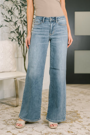 Person wearing light blue flared jeans in a room with a plant and bench.
