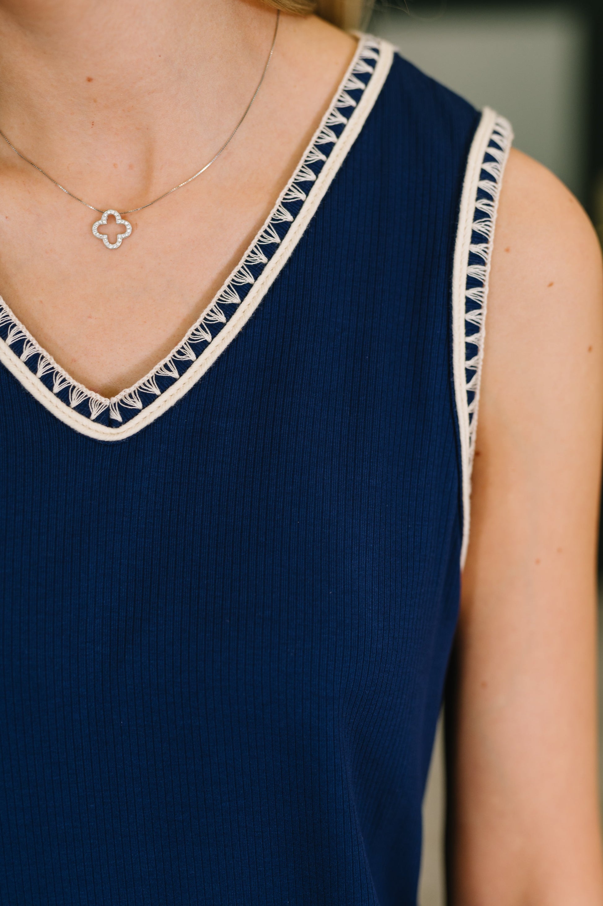 Navy blue sleeveless top with white trim worn by a person, with a blurred background.