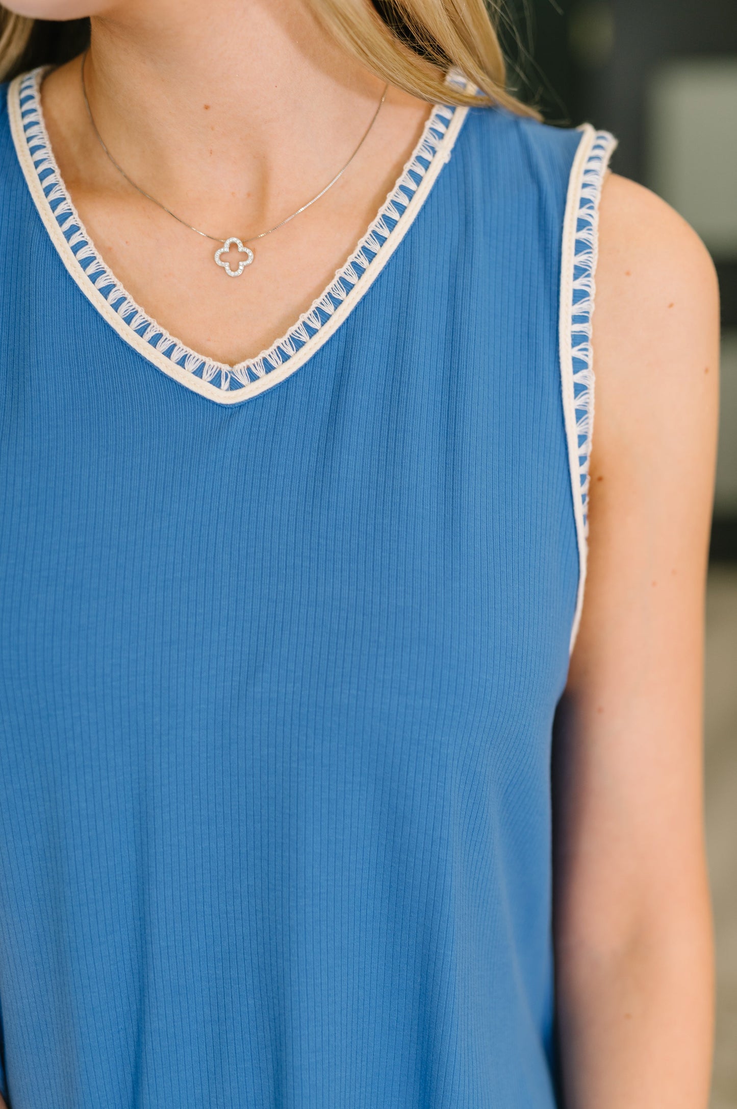 Blue sleeveless top with white trim worn by a person, with a necklace visible.