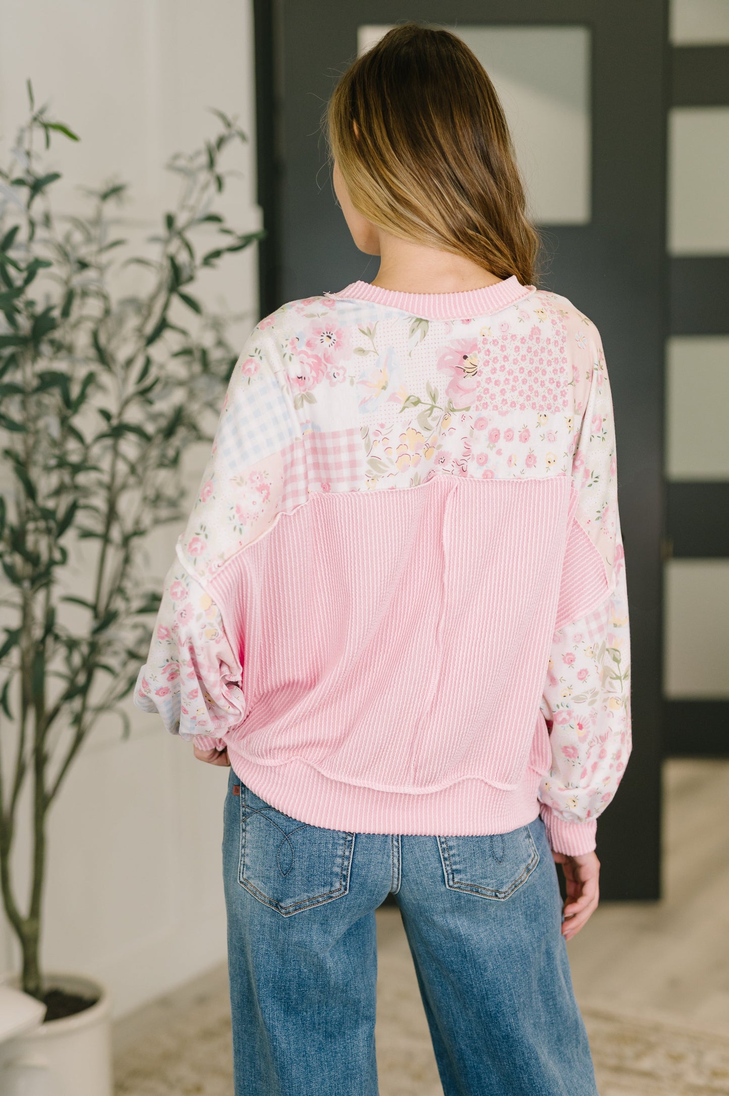 Person wearing a pink floral blouse with blue jeans in an indoor setting