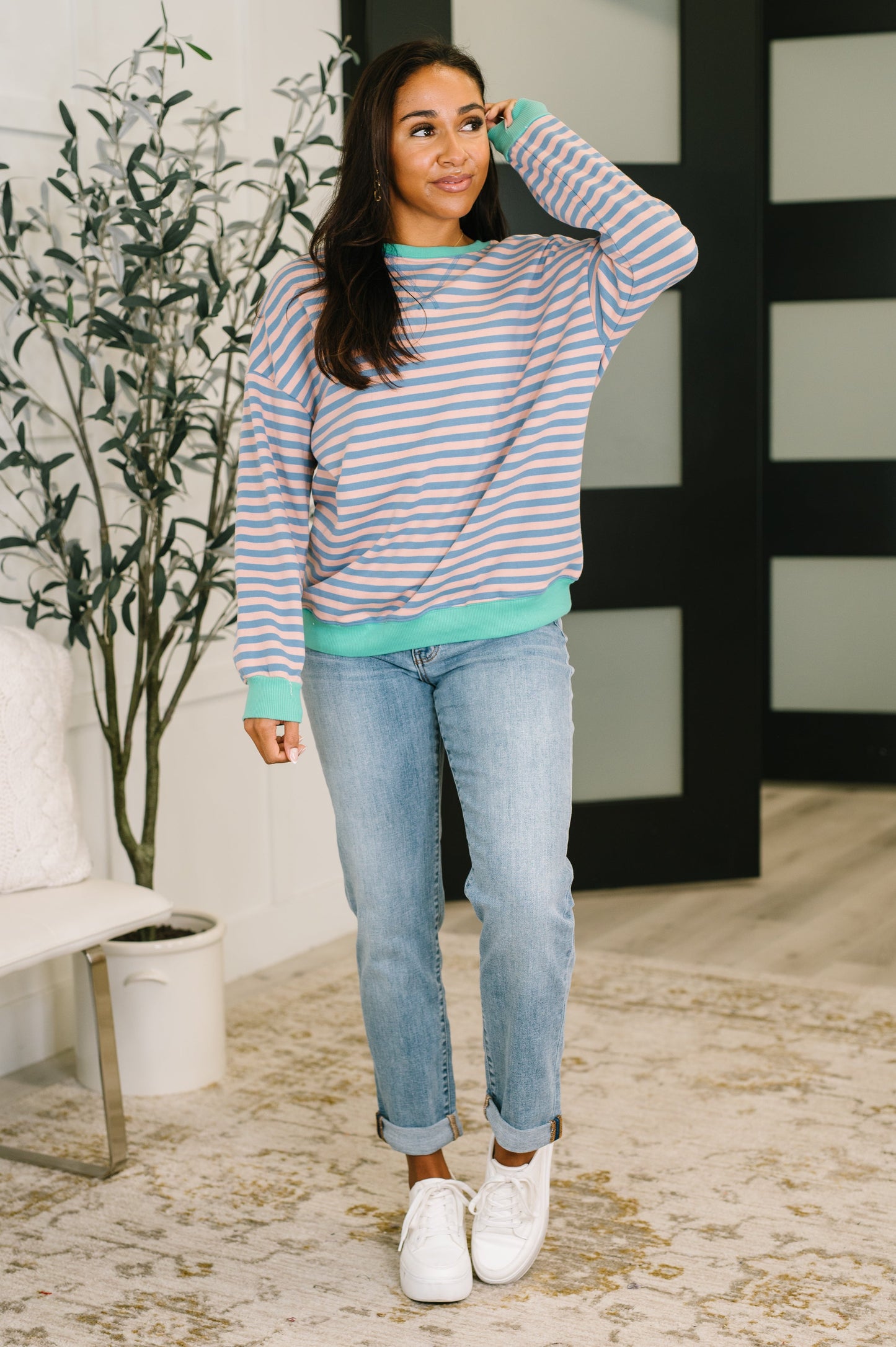 Woman wearing a striped sweater and jeans indoors with a plant in the background