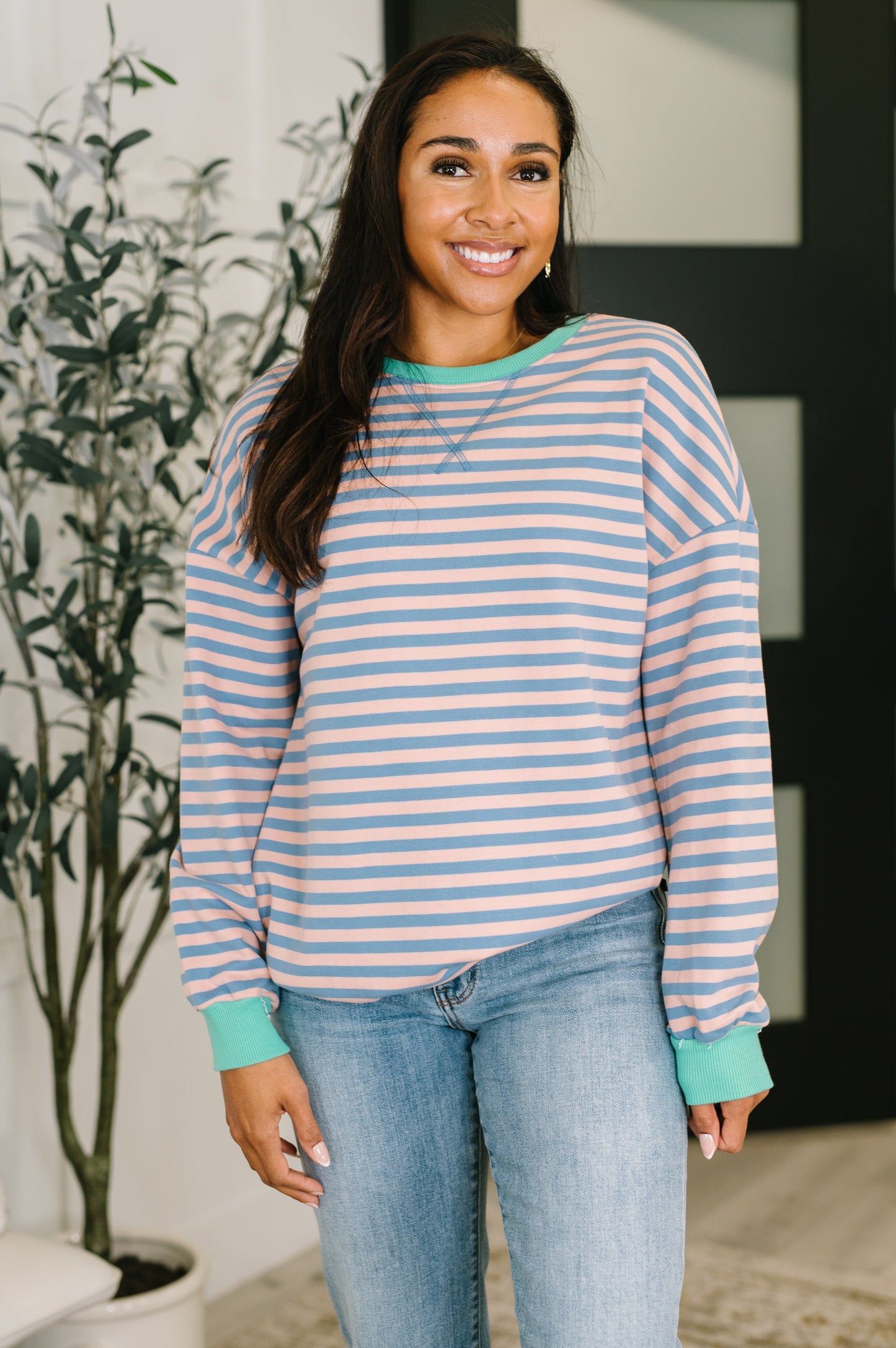 Woman wearing a striped sweater and jeans standing indoors with a plant in the background