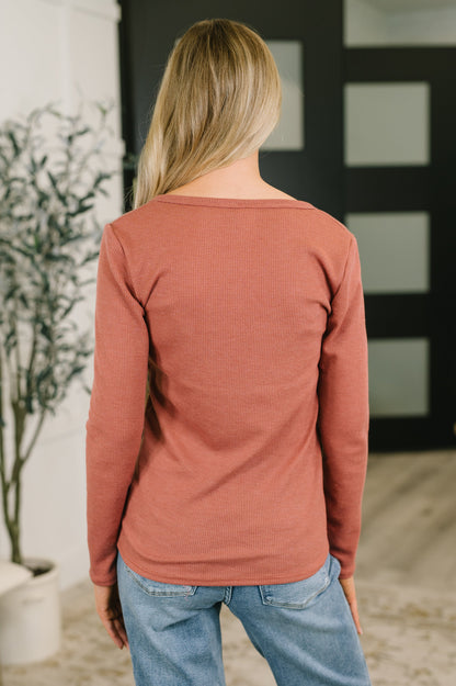 A woman viewed from behind wearing a dusty rose long-sleeve top and blue jeans in an indoor setting.