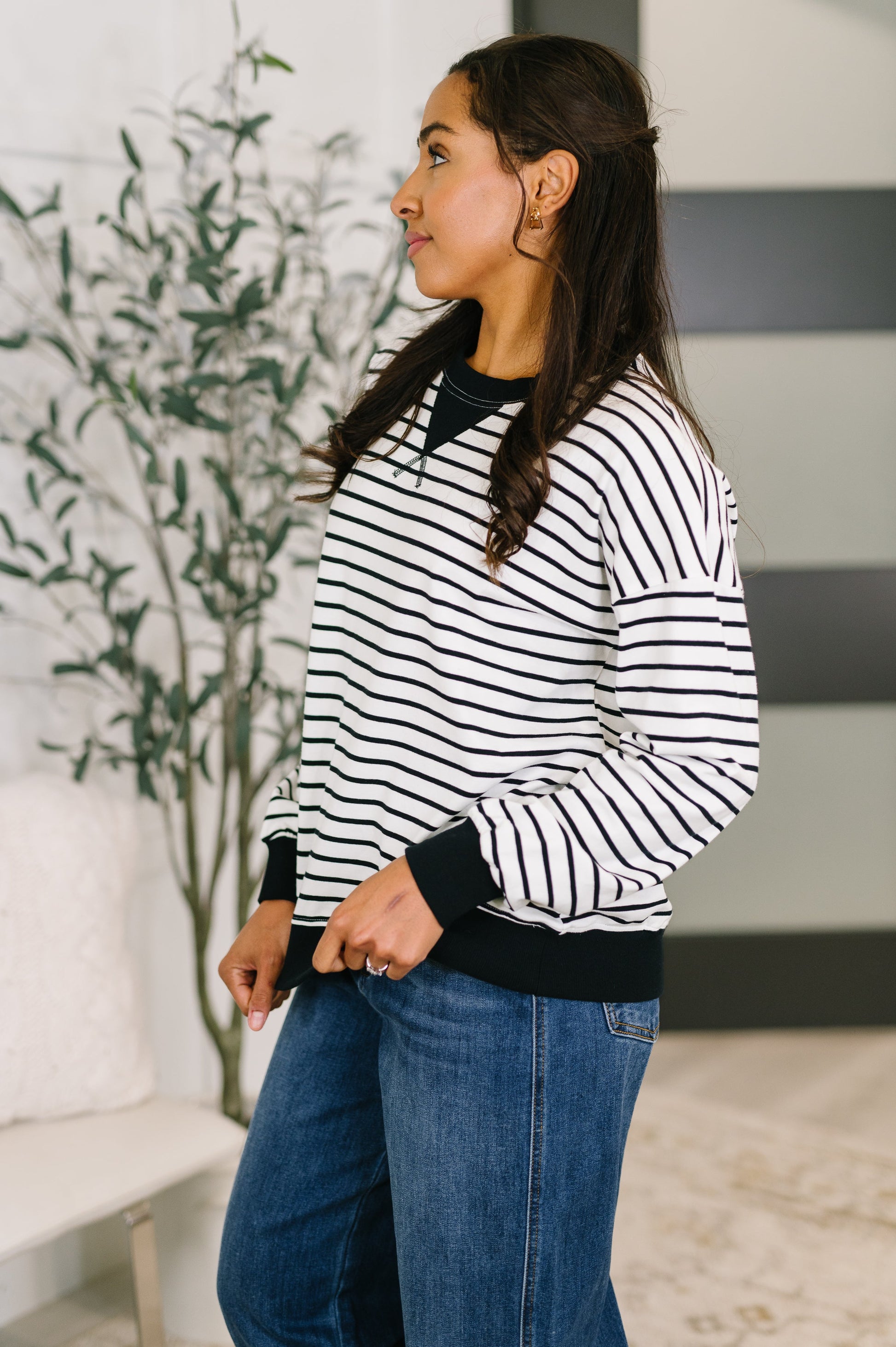 Woman wearing a black and white striped sweater and blue jeans standing indoors.