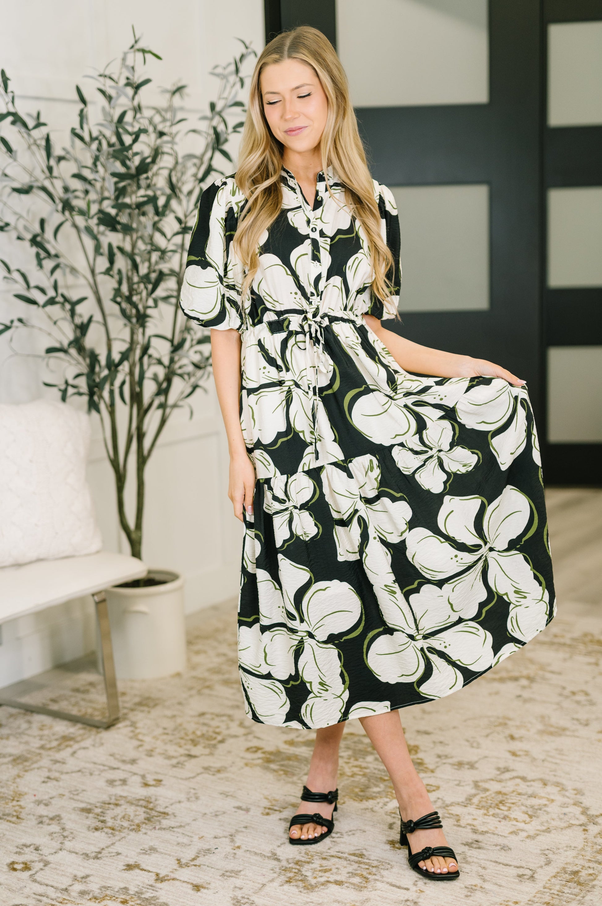 Woman wearing a black and white floral dress in a room with a plant and bench.