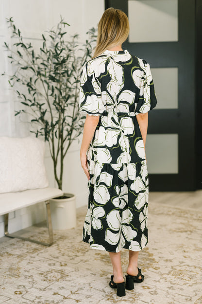 Woman wearing a black and white floral dress in a room with a plant and sofa.