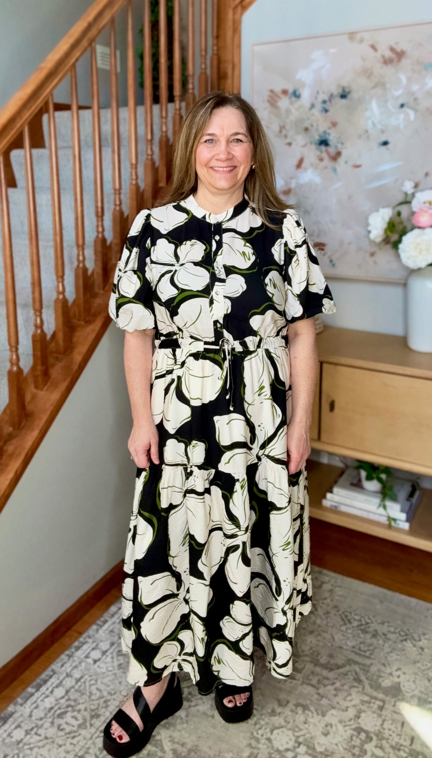Woman wearing a black and white floral dress standing in a home setting.