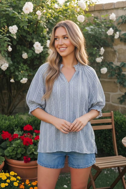 Woman wearing a blue striped shirt and denim shorts standing in a garden.