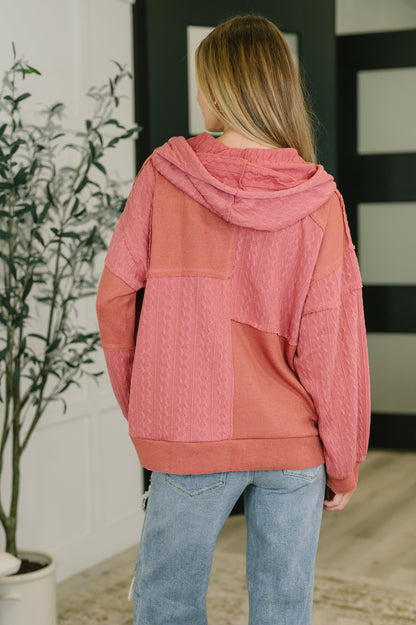Person wearing a pink and coral patchwork hoodie indoors.