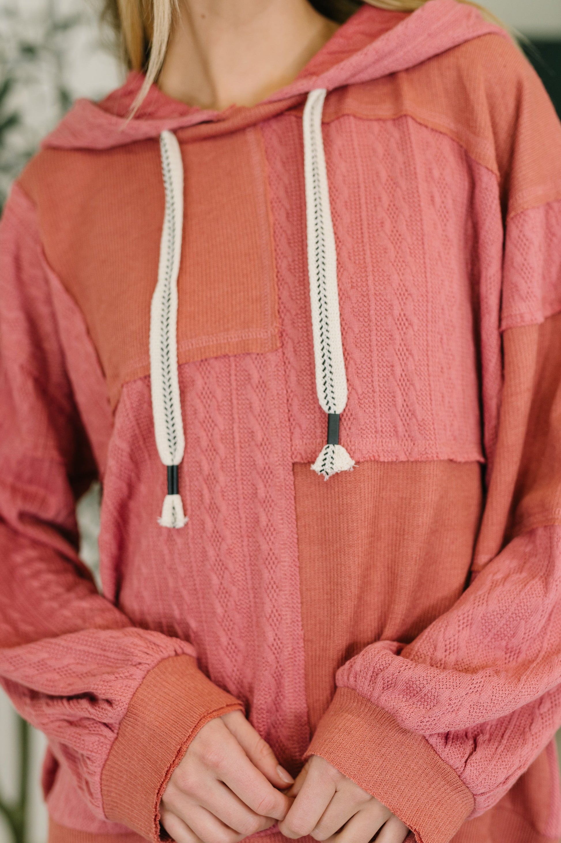Person wearing a pink and brown hooded top with a blurred background
