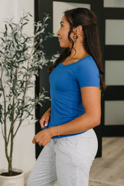 Woman wearing a blue shirt and gray pants standing indoors with a plant in the background