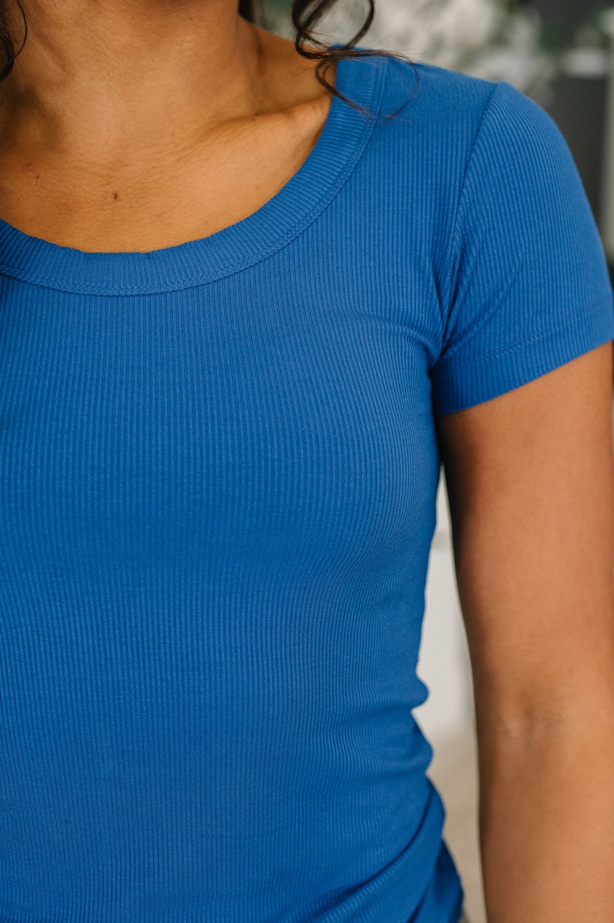 Close-up of a person wearing a blue ribbed shirt with a blurred background