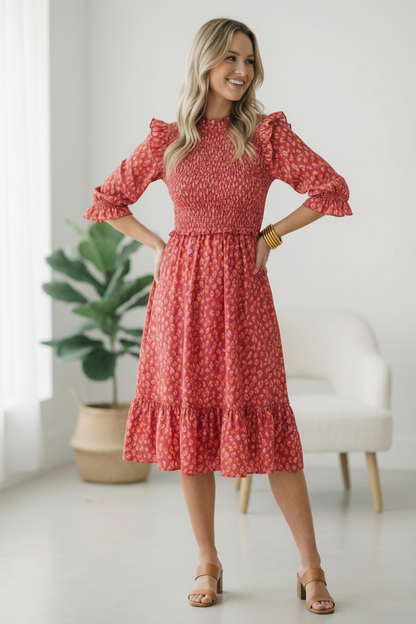 Woman wearing a red floral dress in a bright room with a plant and chair.
