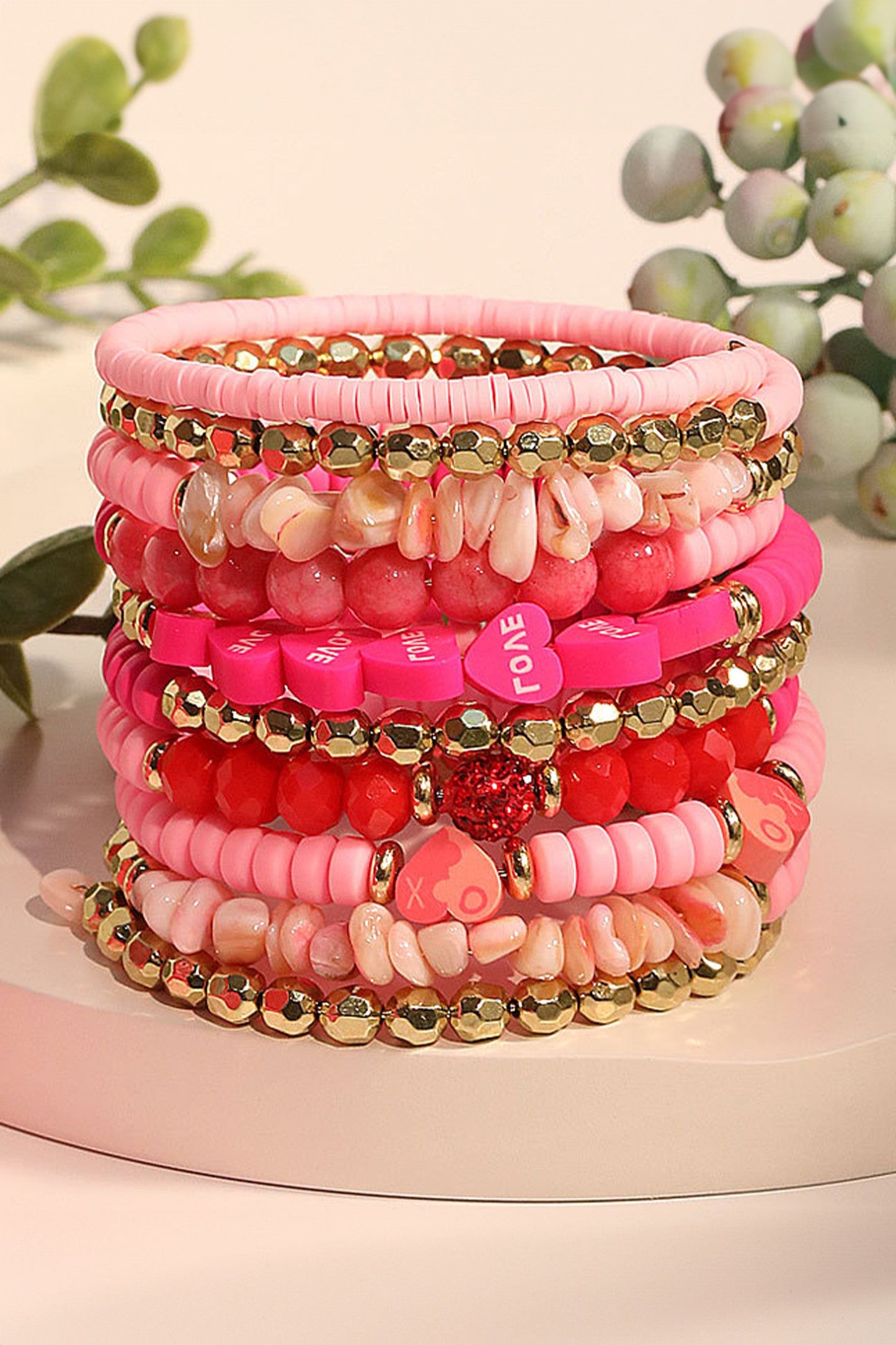 Stack of pink beaded bracelets with heart-shaped charms on a white surface.