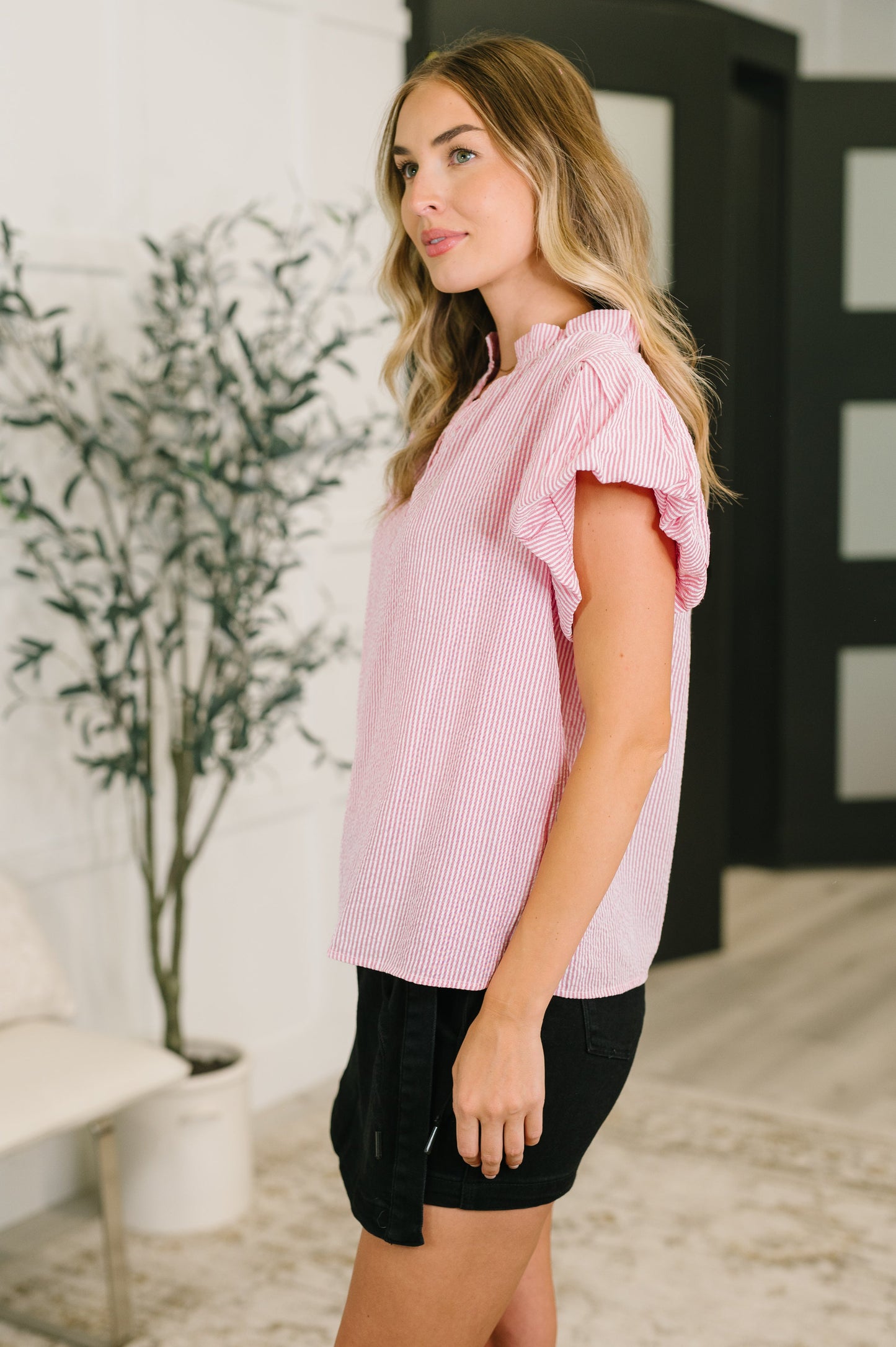 Woman wearing a pink checkered top and black shorts in an indoor setting.