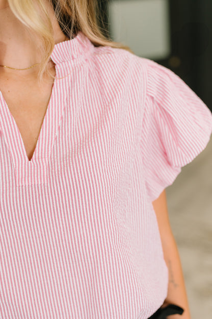 A close-up of a woman wearing a pink and white vertically striped blouse with short puff sleeves and a split V-neckline.