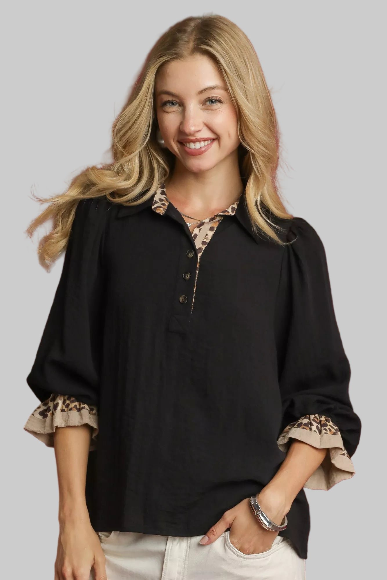 Woman wearing a black half button blouse with beige leopard trim.