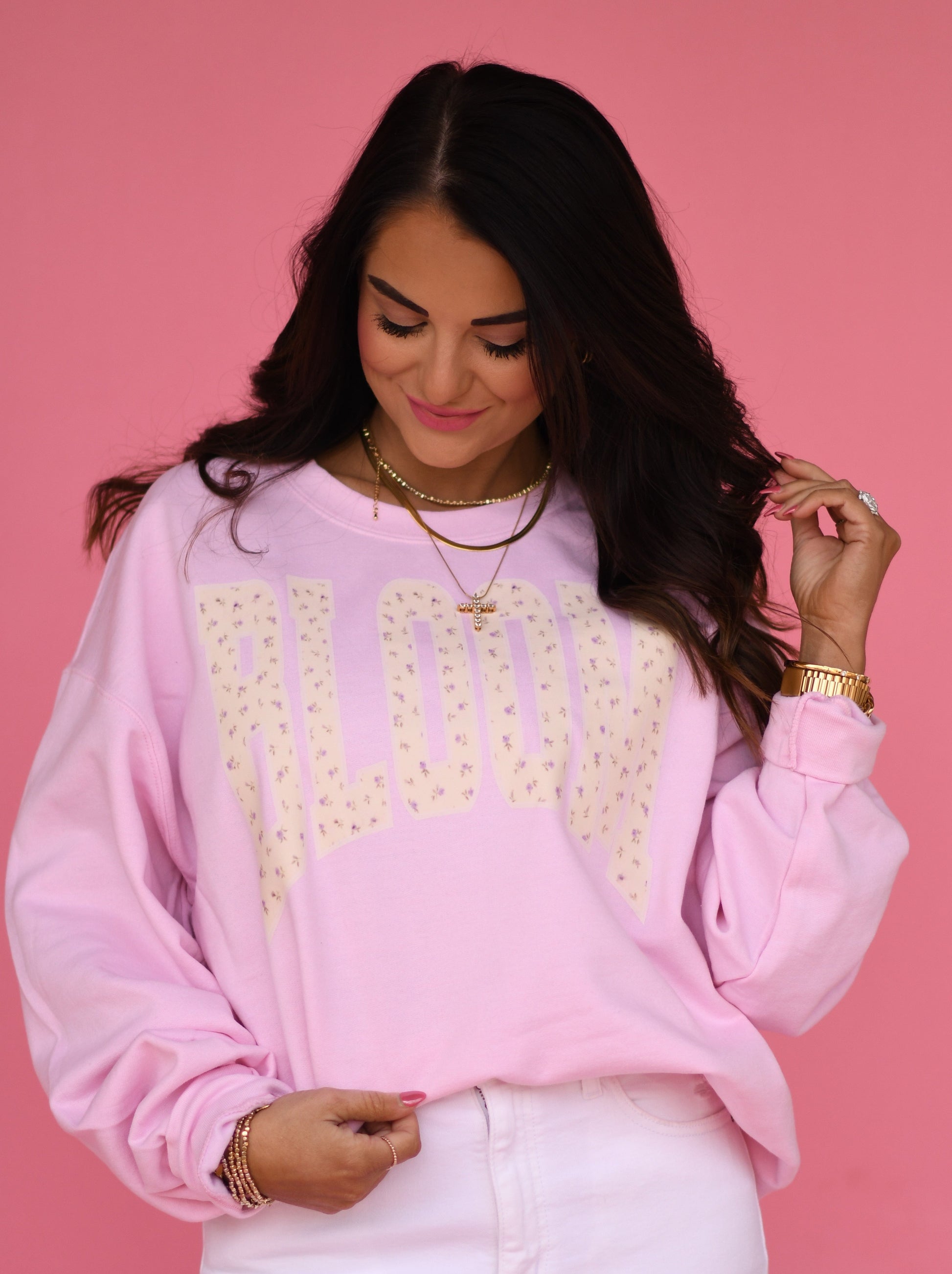 Woman wearing a pink sweatshirt with 'BLOOM' printed on it against a pink background