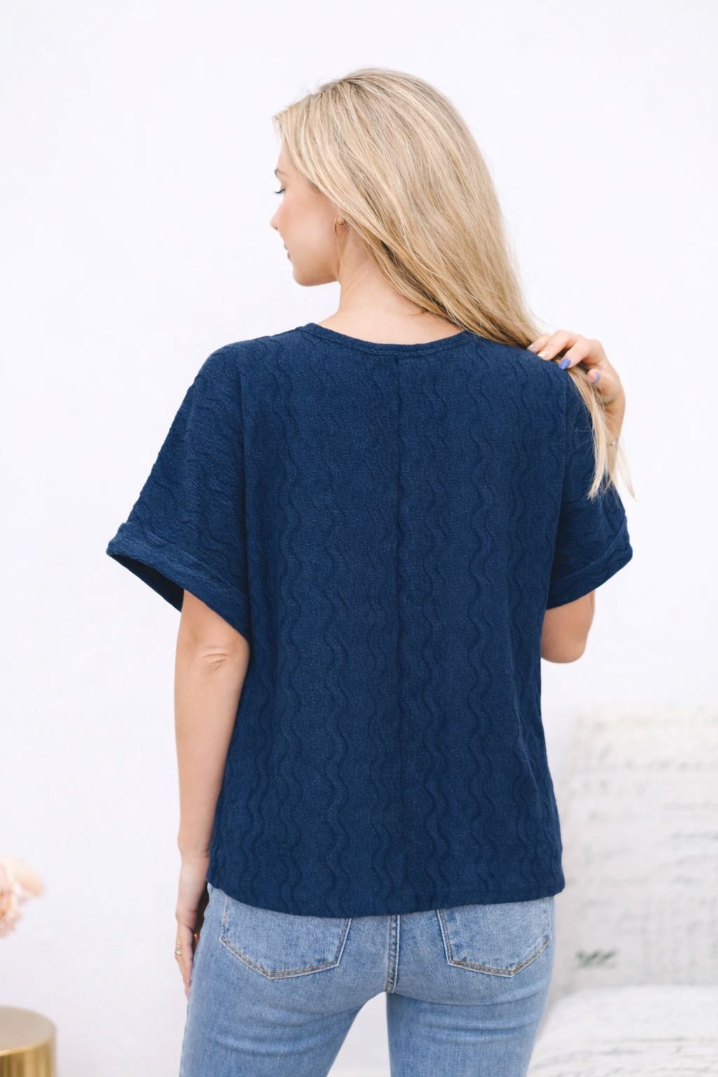 Woman wearing a navy blue cable knit sweater and light blue jeans against a white background