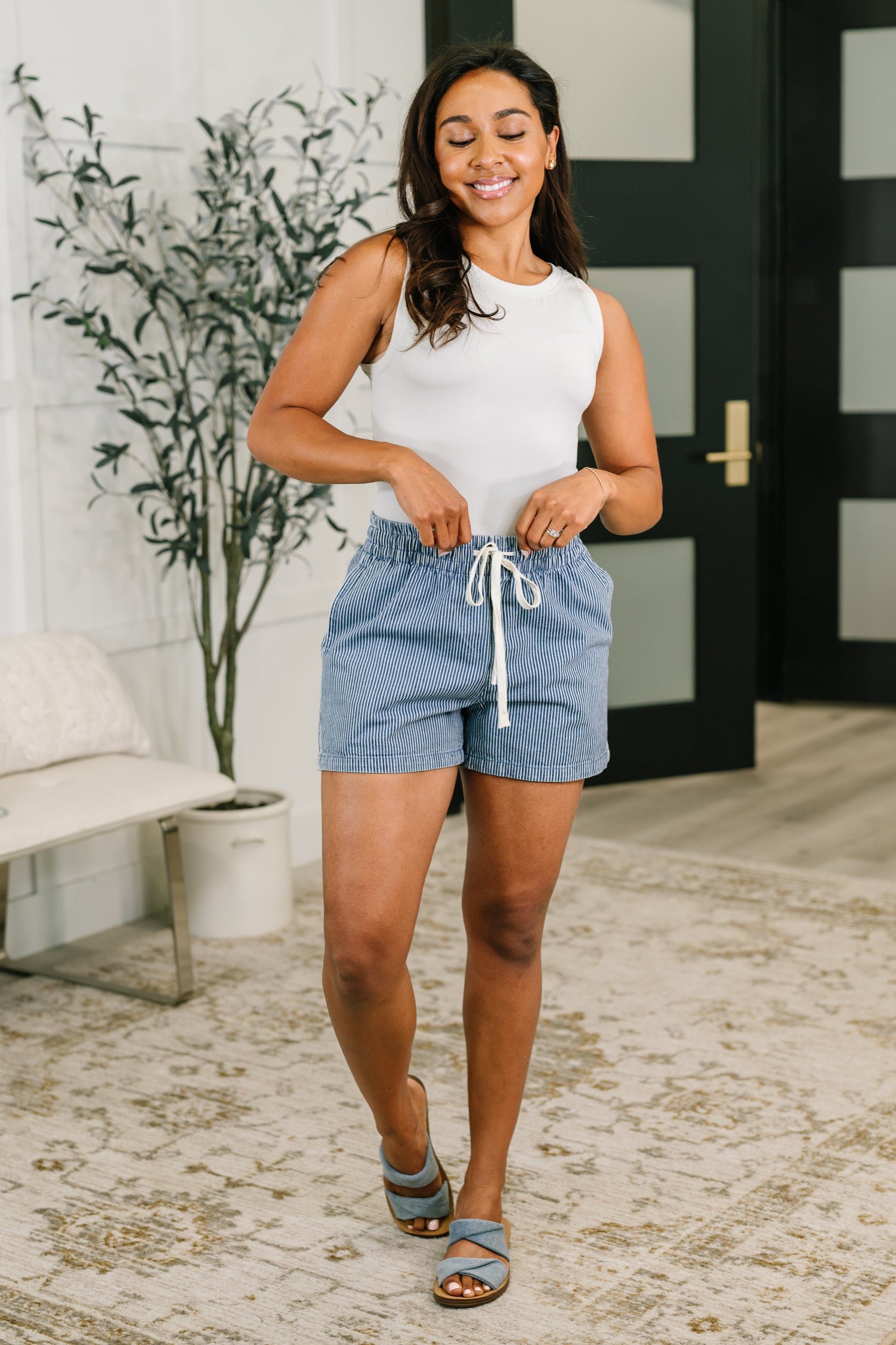 Woman wearing a white tank top and blue shorts in an indoor setting.