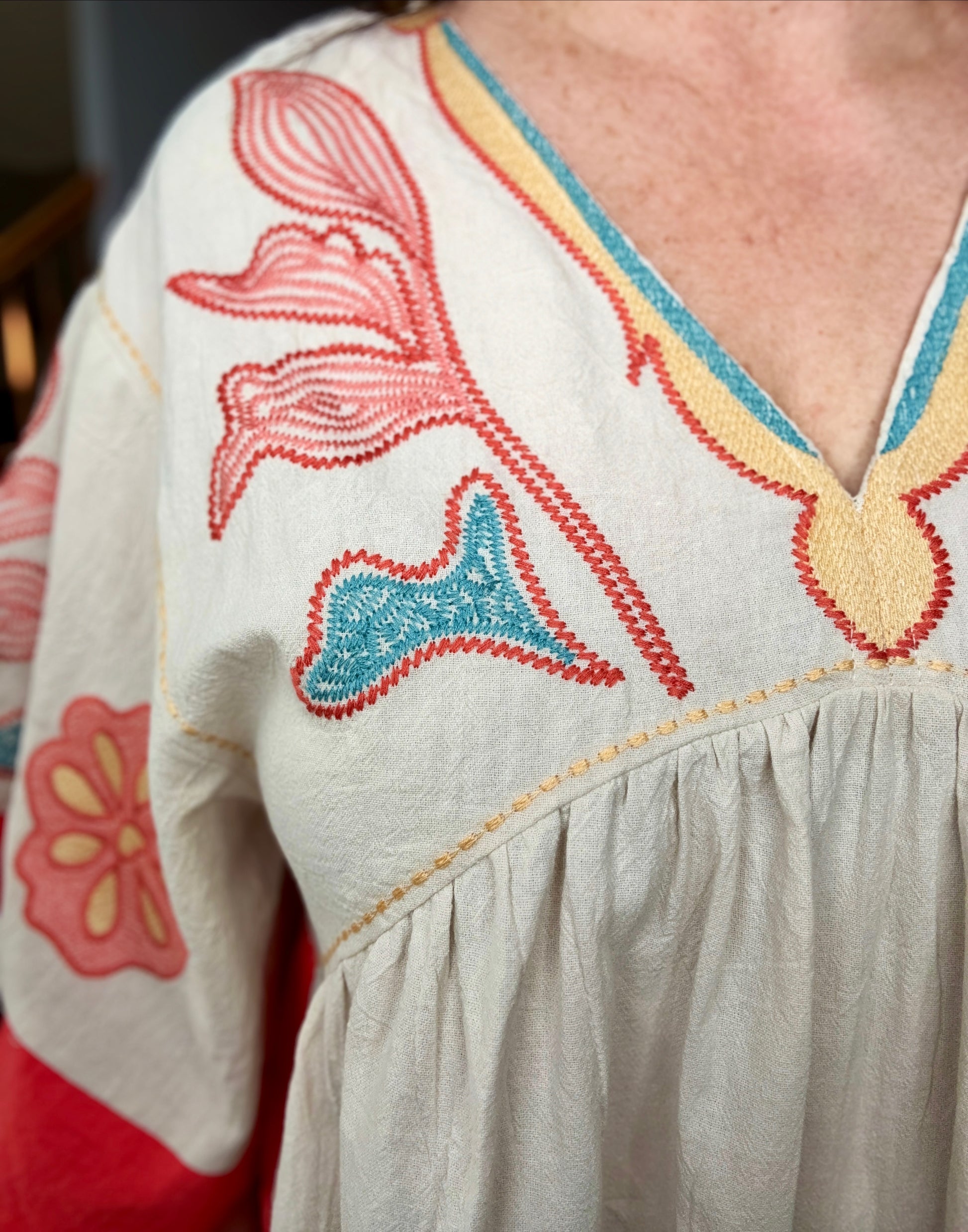 Close-up of a person wearing a light-colored dress with colorful floral embroidery.