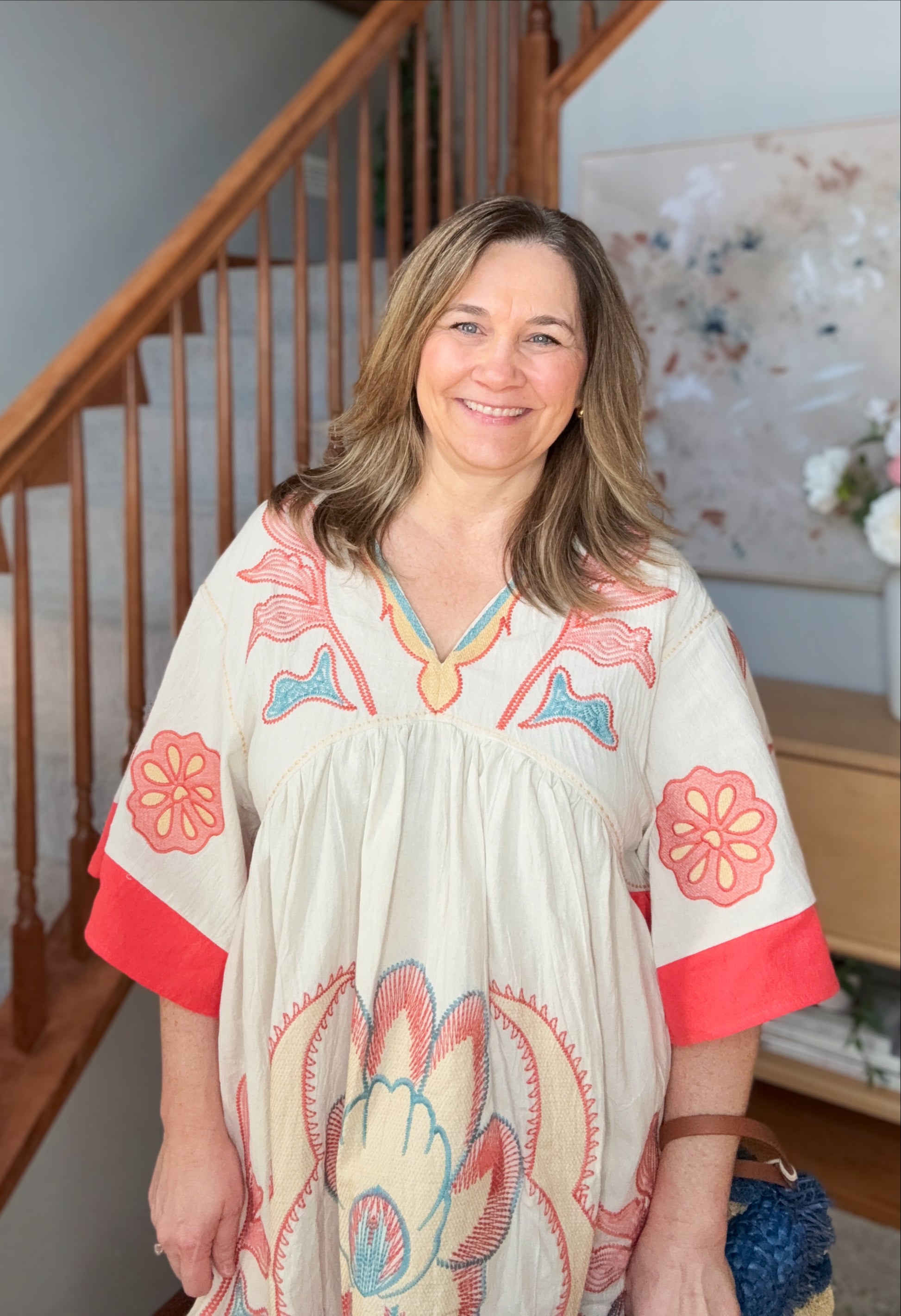 Woman wearing a floral dress with red accents standing in a home setting.