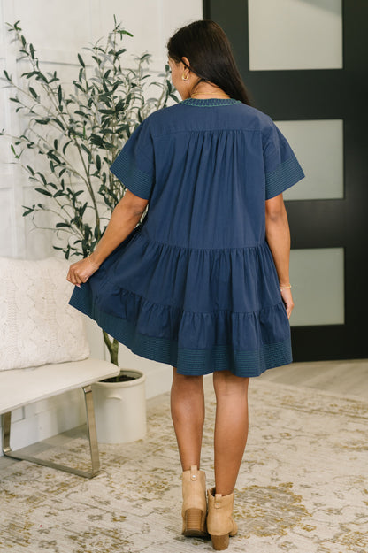 Woman wearing a blue dress in an indoor setting with a plant and white furniture.