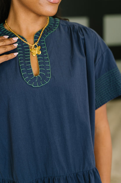 Navy blue dress with green embroidery and gold necklace worn by a person.
