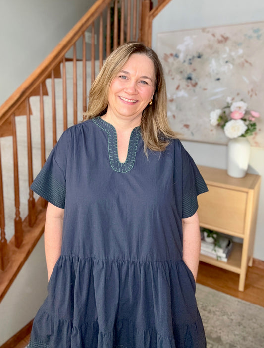 Woman wearing a navy blue dress with green trim in a home setting.