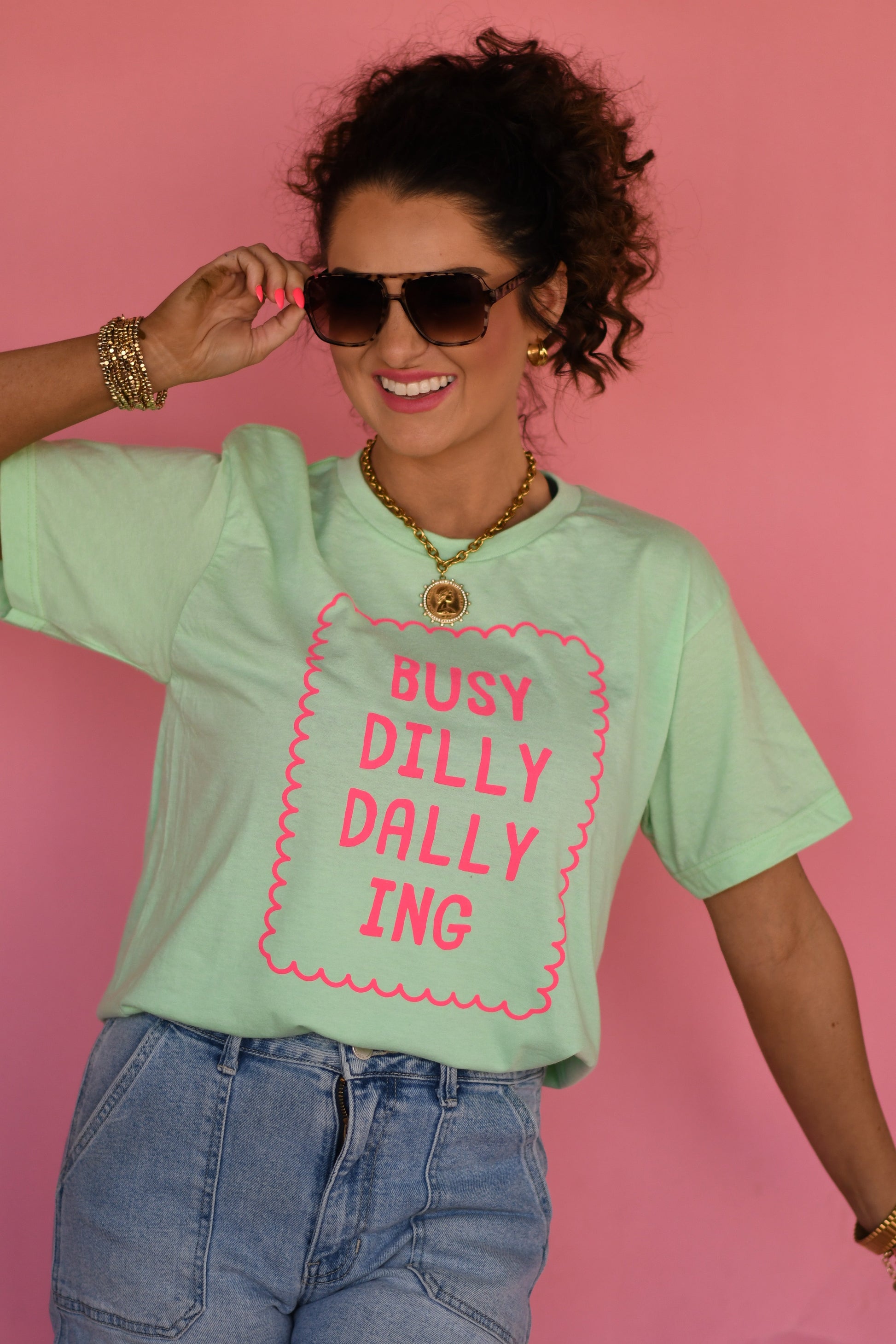 Woman wearing a light green t-shirt with pink text against a pink background