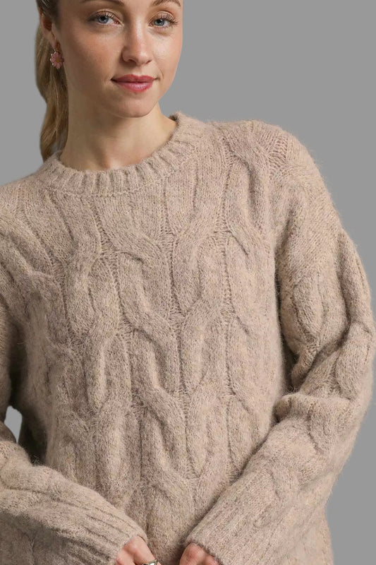 Woman wearing a beige cable knit sweater against a gray background