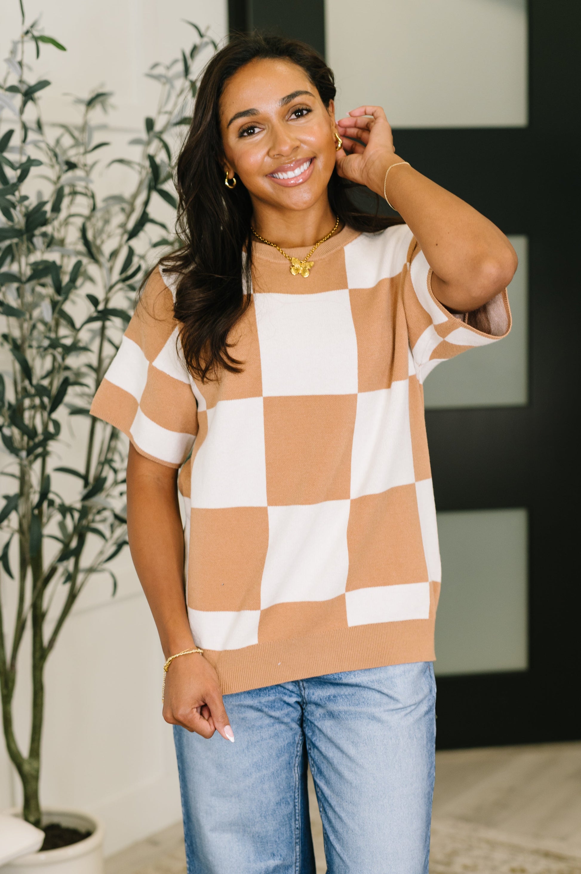 Woman wearing a checkered top and jeans indoors with a plant in the background