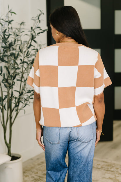 Person wearing a checkered shirt and jeans standing indoors with a plant in the background