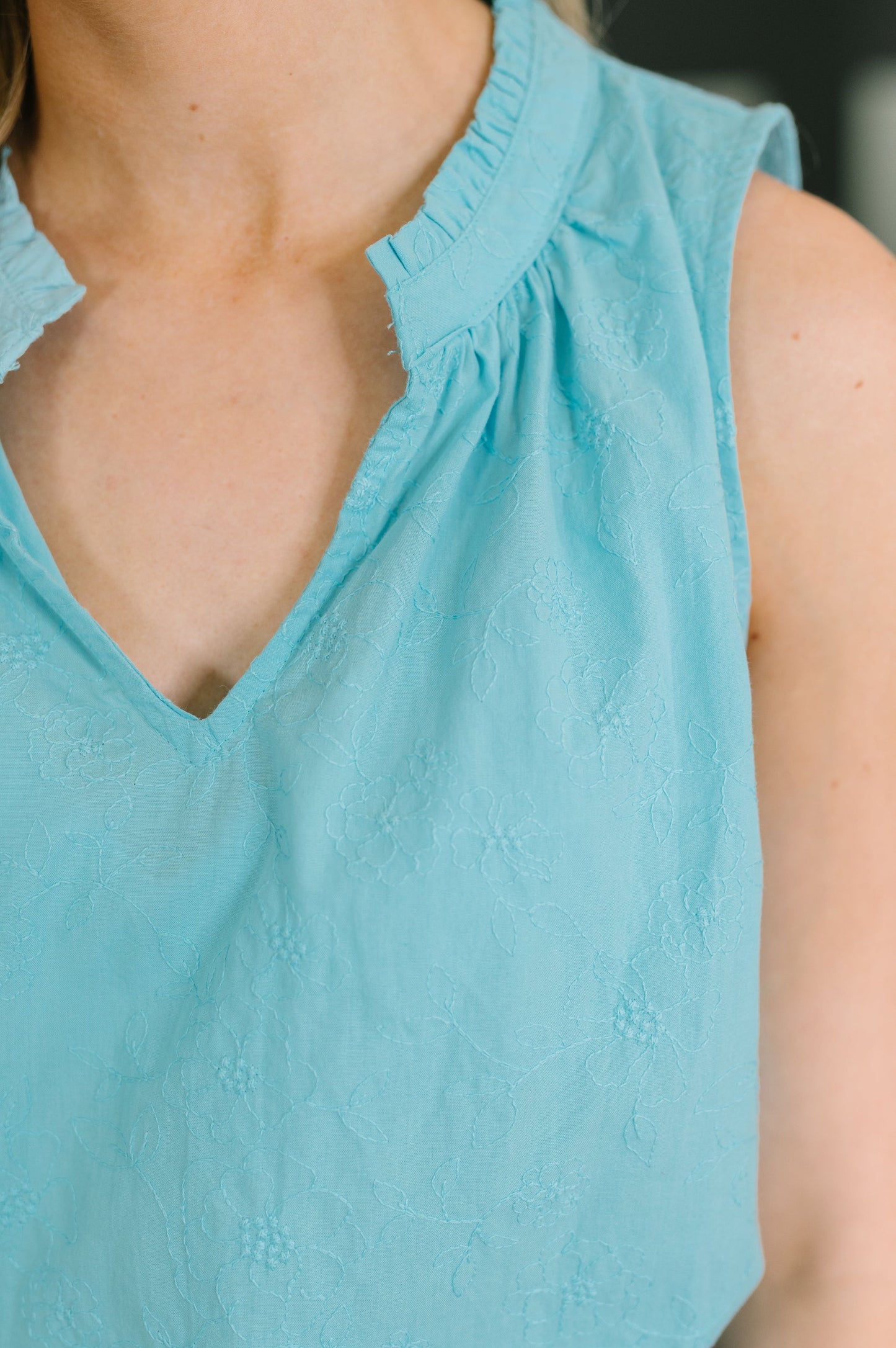 Close-up of a sleeveless light blue eyelet top worn by a model, showing the textured fabric and gathered neckline.