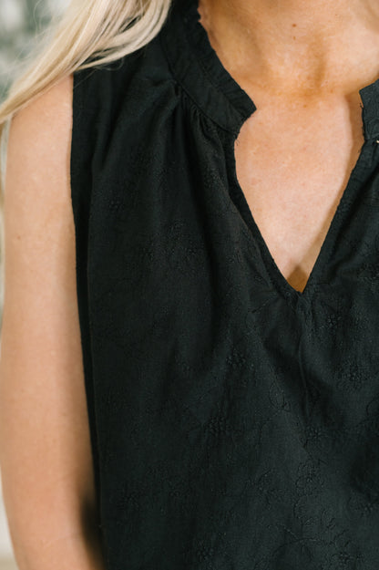 Close-up of a person wearing a black sleeveless top with a gathered high neckline and a split V-neckline.