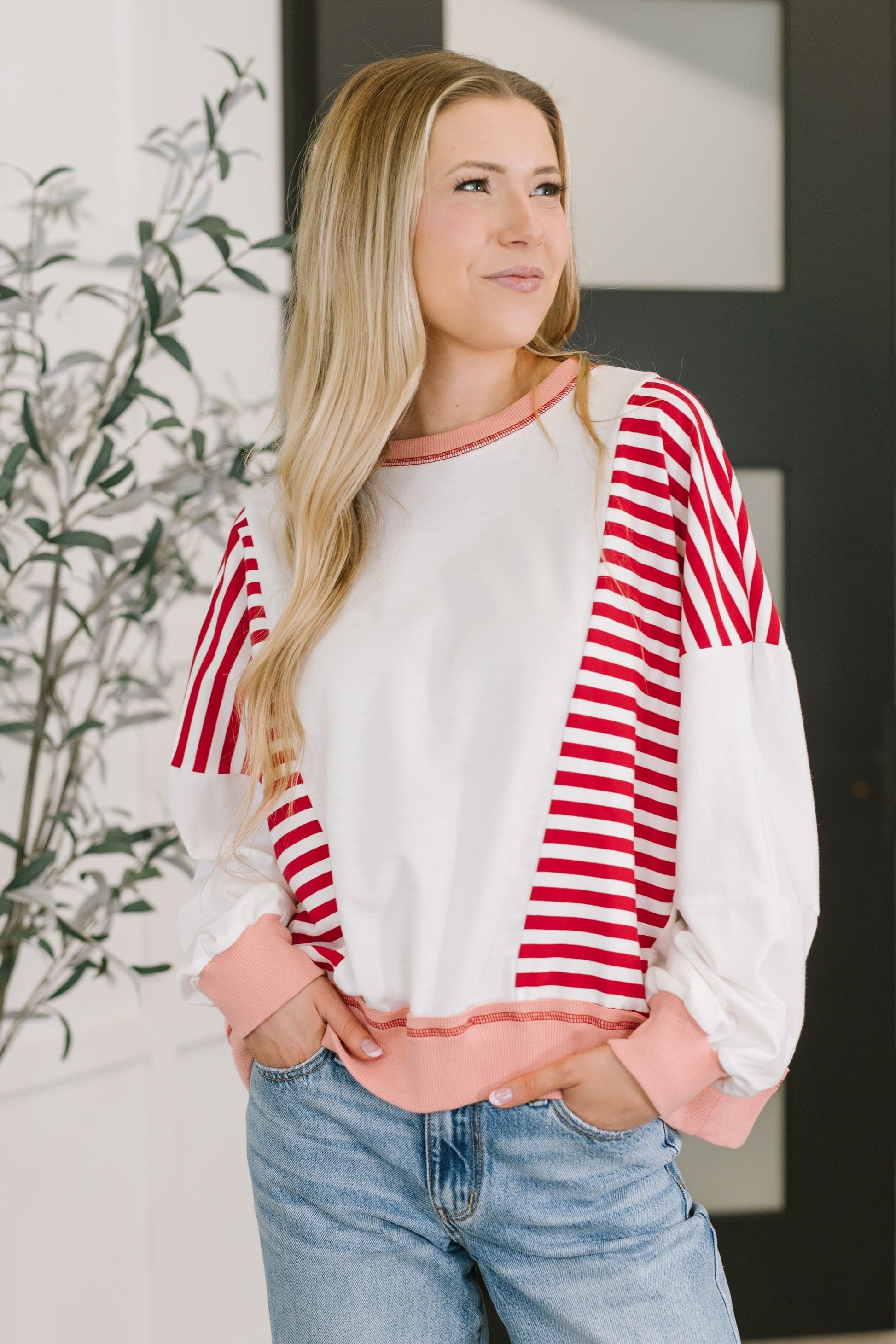 Woman wearing a red and white striped sweater with pink sleeves and collar, standing indoors.