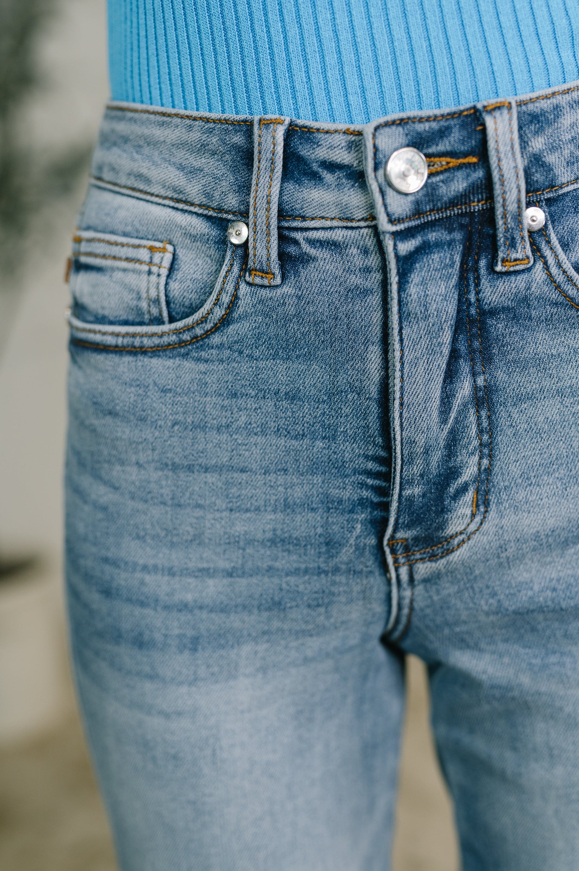 Close-up of a person wearing light blue denim jeans with a bright blue ribbed top visible at the waistband.