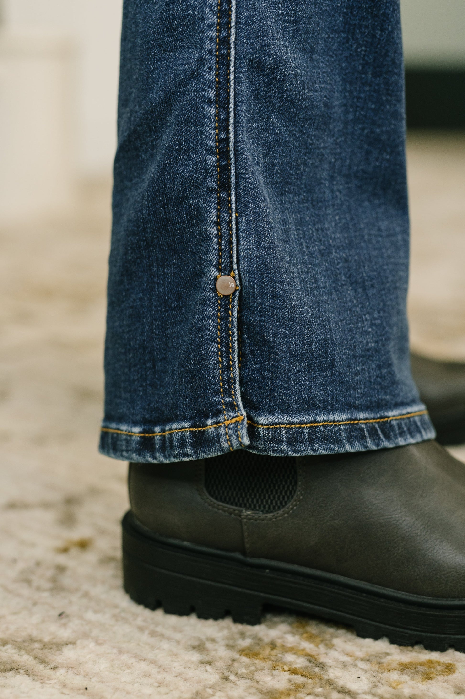 Close-up of blue jeans with a button and black shoes on a textured surface