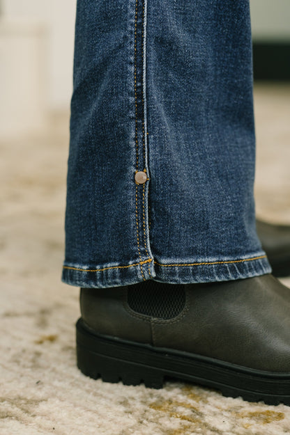Close-up of blue jeans with a button and black shoes on a textured surface