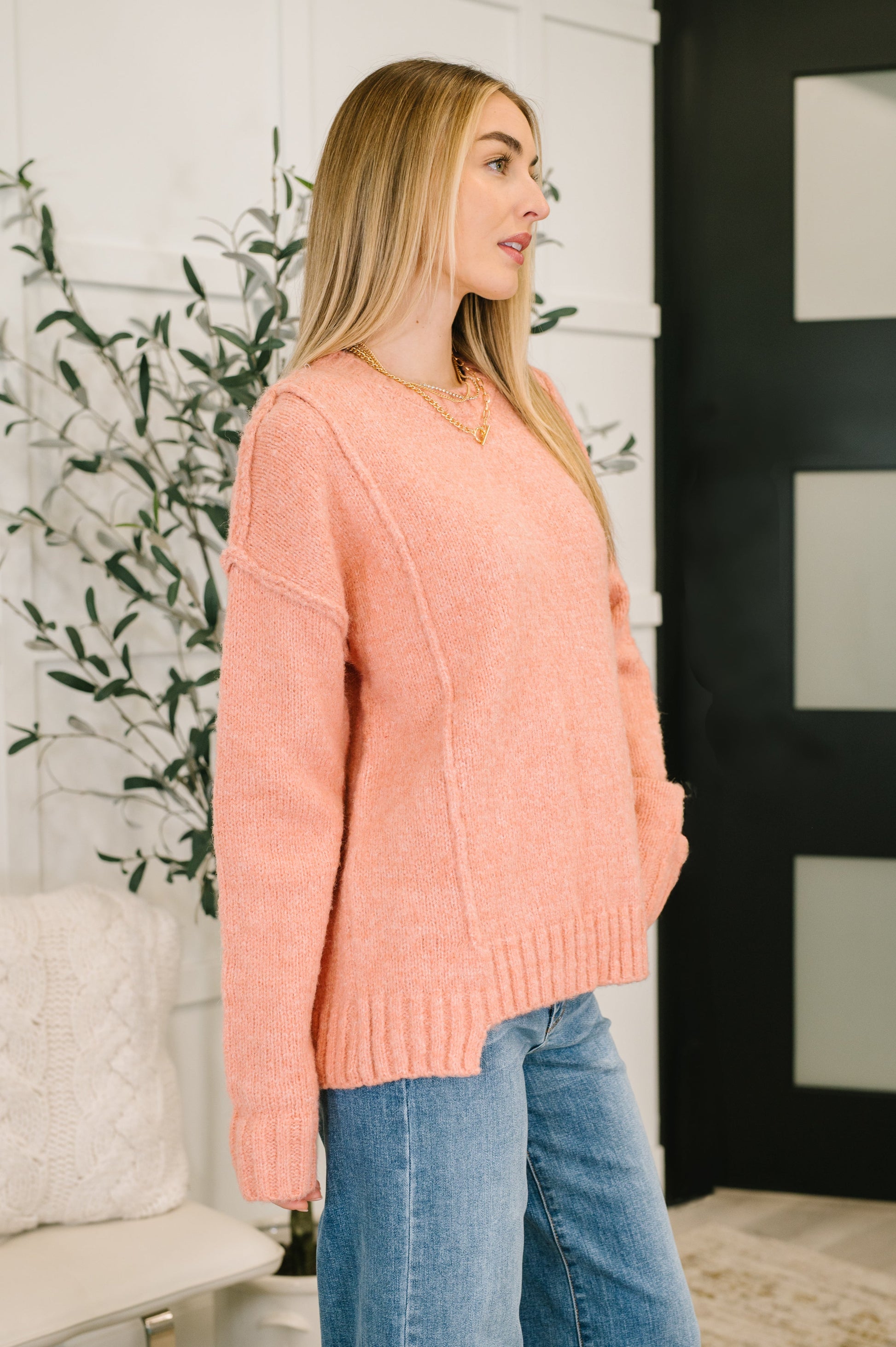 Woman wearing a pink sweater and blue jeans standing indoors with decorative elements.
