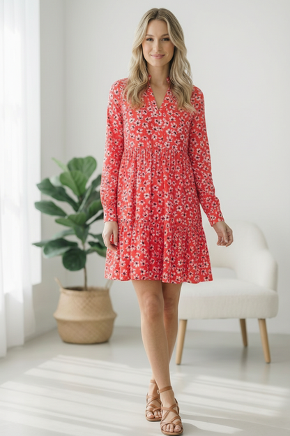 Woman wearing a red floral dress in a bright room with a plant and chair.