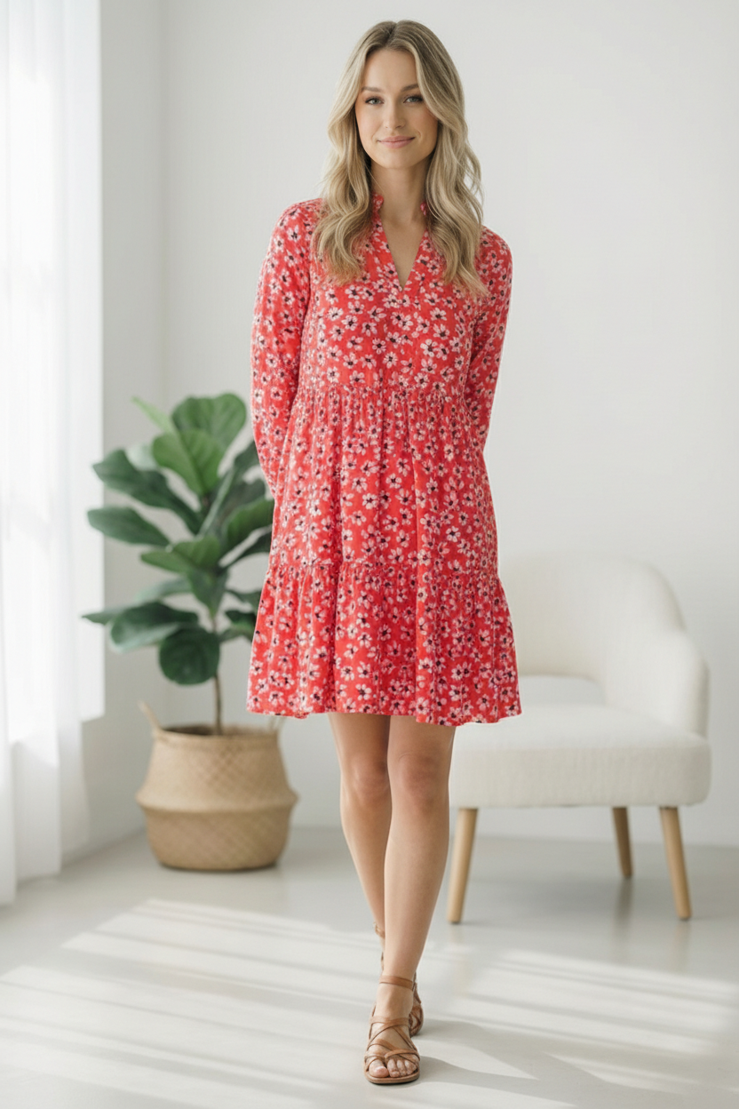 Woman wearing a red floral dress standing in a bright room with a plant and chair.
